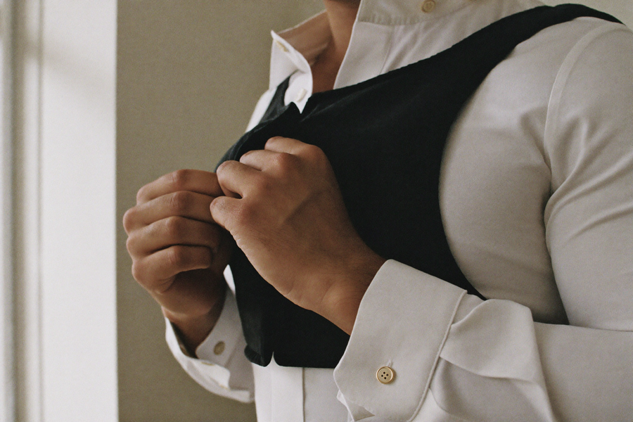 Hands buttoning a white dress shirt over a black compression base layer, brand close-up