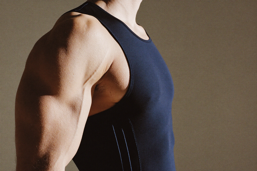 Side profile of a man in a fitted black compression vest, clean chest line, no model face visible