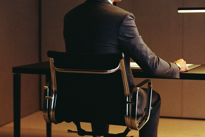 Man in dark suit at executive desk, evening light, still upright at the end of a long day
