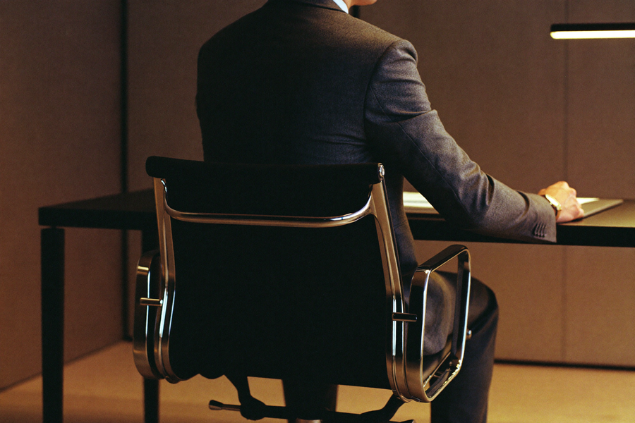 Man in dark suit at executive desk, evening light, still upright at the end of a long day