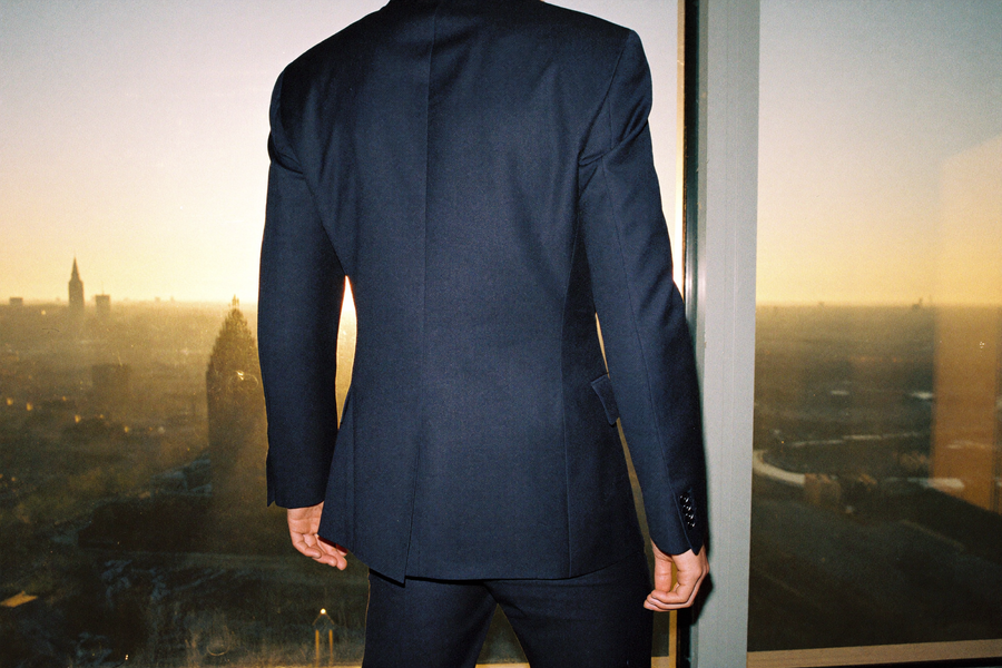 Anonymous man in tailored navy suit standing at a window, morning light, calm