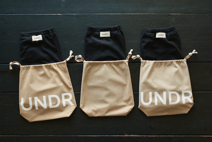Stack of UNDR garments in linen drawstring bags, editorial flatlay