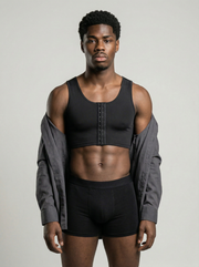 Man wearing a black sports bra and shorts with a gray shirt over his shoulder on a plain background