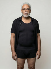 Man wearing a black shirt and black underwear against a plain background