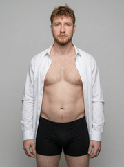 Man wearing a white shirt over black underwear against a gray background