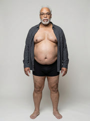 Man wearing a gray cardigan over black underwear on a plain background