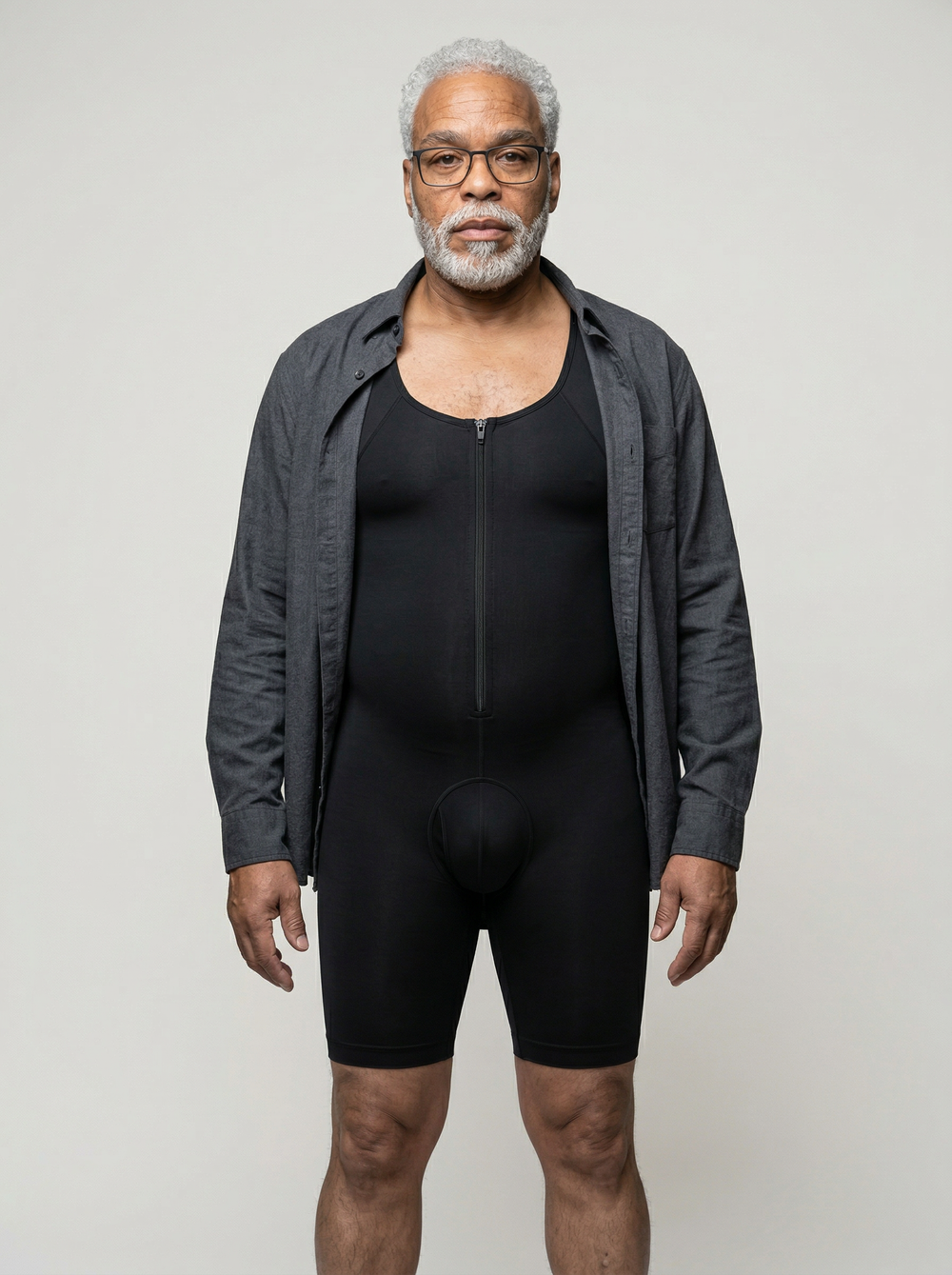 Man wearing a black bodysuit with a gray jacket over it on a plain background