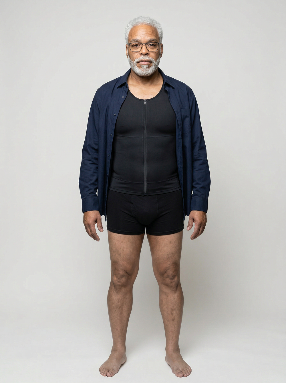 Man wearing a navy jacket over a black shirt and black shorts on a white background