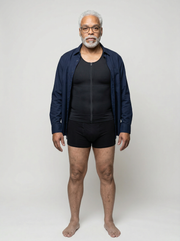 Man wearing a navy jacket over a black shirt and black shorts on a white background